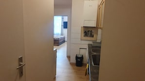 Ein schmaler Flur führt zu einem Schlafzimmer mit Bett und Fenster. Ein Küchenbereich ist sichtbar, mit Spüle und Schränken.
