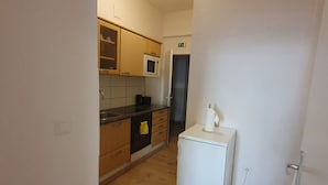 Eine kleine Küche mit Holzausstattung, einer Mikrowelle, einem weißen Kühlschrank und einem sichtbaren Fluchtwegweiser.