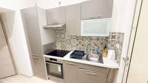 A compact kitchen with a stove, oven, sink, and a window with blinds. - Chic 1BR Apt Near Biggest Amusementpark of Vienna (Vienna)