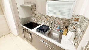 A compact kitchen with a stove, sink, and a window with blinds. - Chic 1BR Apt Near Biggest Amusementpark of Vienna (Vienna)