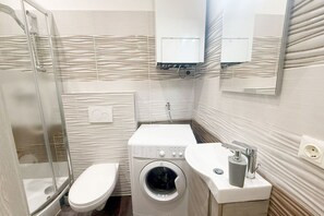 Une petite salle de bain dotée d’une douche à parois de verre, de toilettes, d’un lave-linge et d’un lavabo avec un robinet.