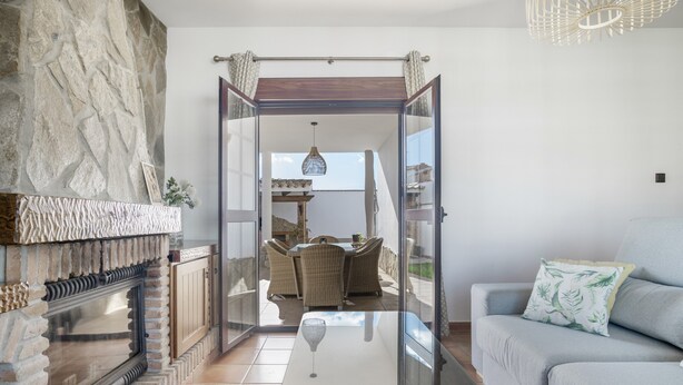 A living room with a fireplace, a glass coffee table, a sofa, and a view to an outdoor dining area. - Holiday Home 'Villa' with Private Pool, Wi-Fi and Air Conditioning (Conil de la Frontera)