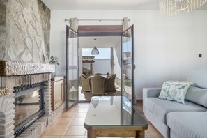 A living room with a fireplace, a glass coffee table, a sofa, and a view to an outdoor dining area. - Holiday Home 'Villa' with Private Pool, Wi-Fi and Air Conditioning (Conil de la Frontera)