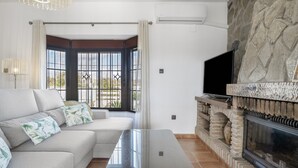 A living room with a sofa, a glass-top coffee table, a stone fireplace, and a television. - Holiday Home 'Villa' with Private Pool, Wi-Fi and Air Conditioning (Conil de la Frontera)