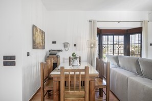 A dining area with a wooden table and chairs, a sofa, a painting, a telephone, and a window with curtains. - Holiday Home 'Villa' with Private Pool, Wi-Fi and Air Conditioning (Conil de la Frontera)