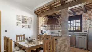 A dining area with a glass table and wooden chairs, a brick kitchen with a chimney, and a refrigerator. - Holiday Home 'Villa' with Private Pool, Wi-Fi and Air Conditioning (Conil de la Frontera)