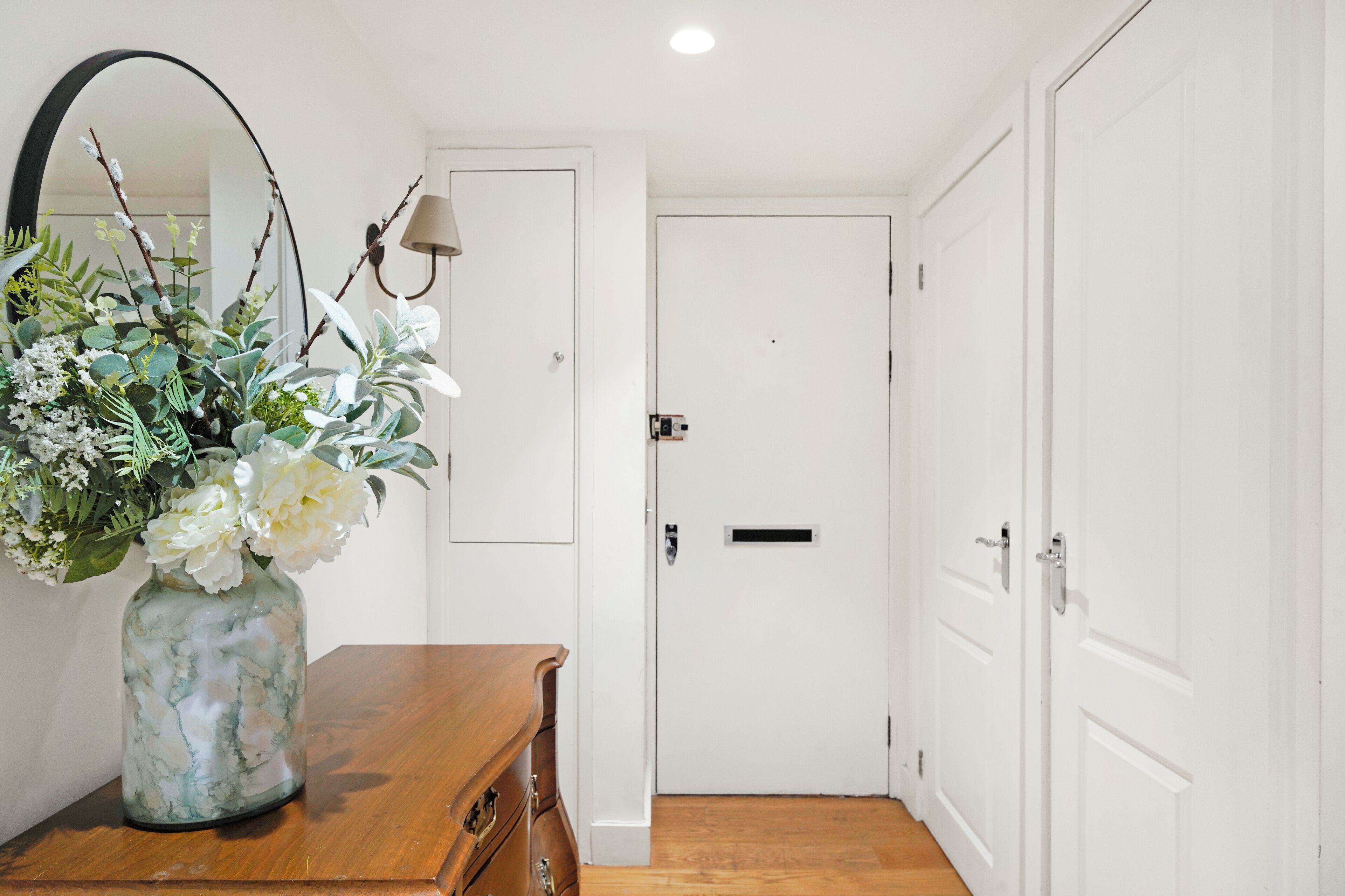 A hallway with a wooden dresser, a vase of flowers, a mirror, and white doors.