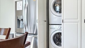 A kitchen with a stainless steel refrigerator, a built-in washing machine, and a wooden dining table.