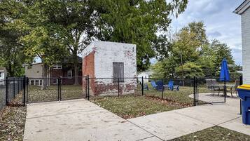 A fenced outdoor area with a small brick structure, a concrete pathway, and blue chairs.