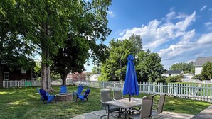 A patio with a table and chairs, a blue umbrella, and a stone fire pit.