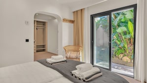 Ein modernes Hotelzimmer mit einem großen Bett, einem Korbstuhl und einer Glasschiebetür, die zu einem Garten führt.