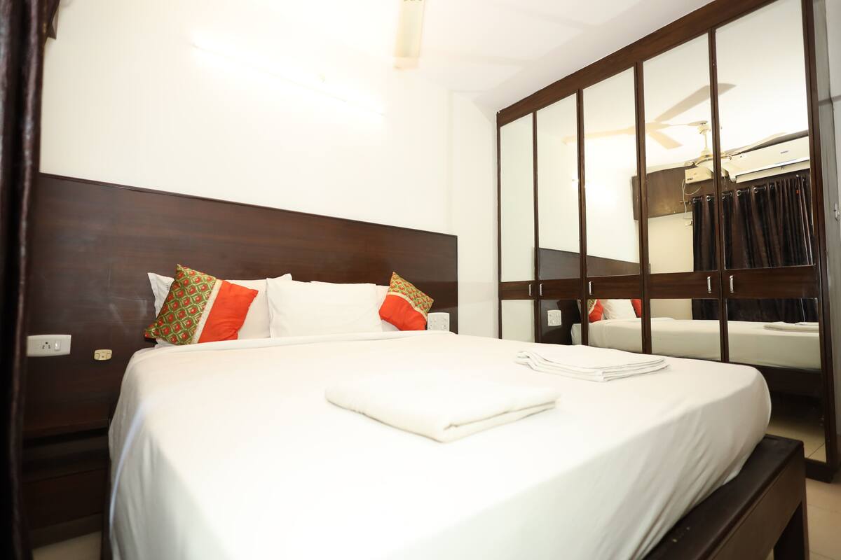A hotel room with a large bed, a wardrobe with a mirror, and a ceiling fan.