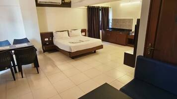 Una habitación de hotel con cama, escritorio con sillas, una pequeña kitchenette y baño.