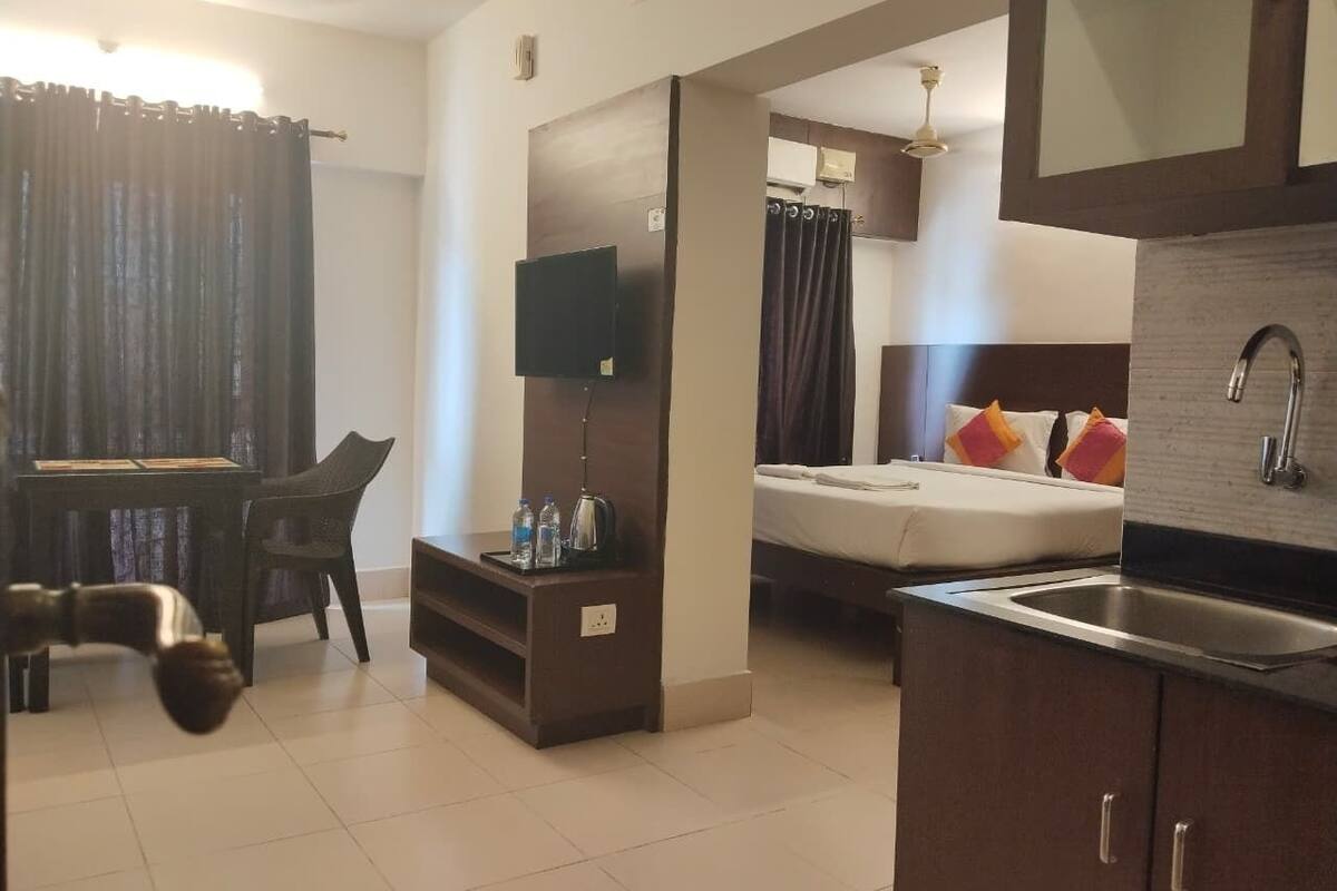 A hotel room with a bed, a desk, a TV, a small kitchenette, and a bathroom.