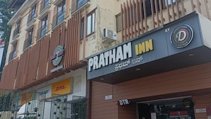 Ένα κτίριο με μια πινακίδα που αναγράφει «Pratham Inn», ένα σημείο εξυπηρέτησης της DHL και μια πινακίδα που δείχνει το «Down the Road Kitchen».