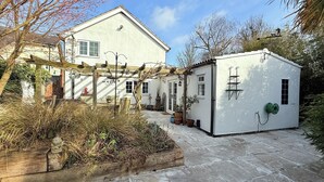 Un edificio bianco con un patio piastrellato, una pergola in legno e piante in vaso.