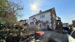 Una casa a due piani con giardino, una carriola e un'auto parcheggiata.