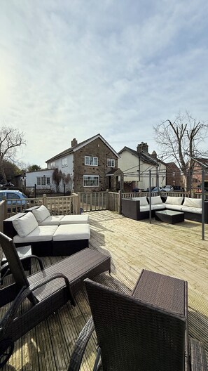 Un espace extérieur aménagé avec des meubles en osier, une terrasse en bois et, en arrière-plan, un bâtiment en pierre.