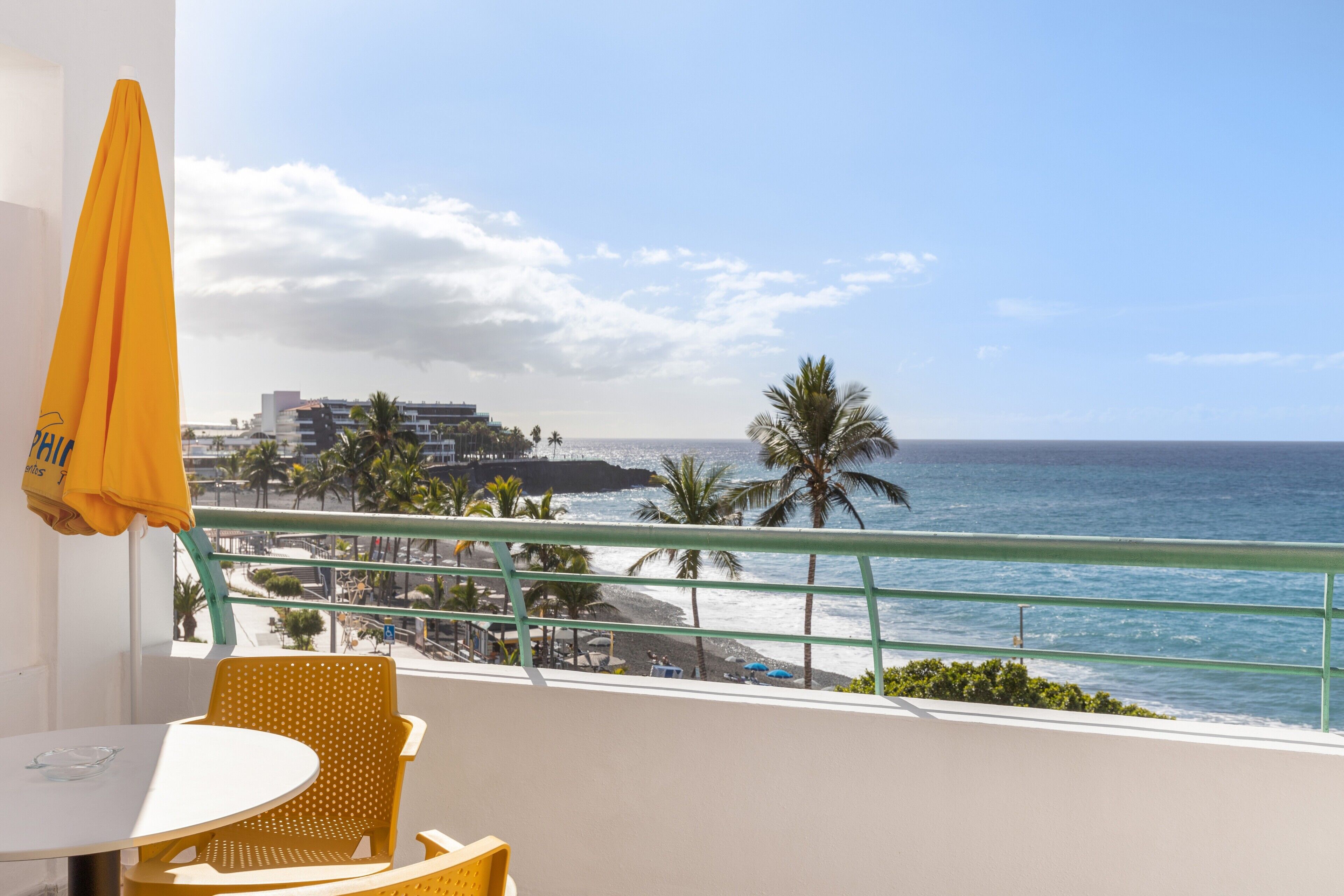 Ein Balkon mit Blick auf das Meer, einem Tisch und gelben Stühlen.