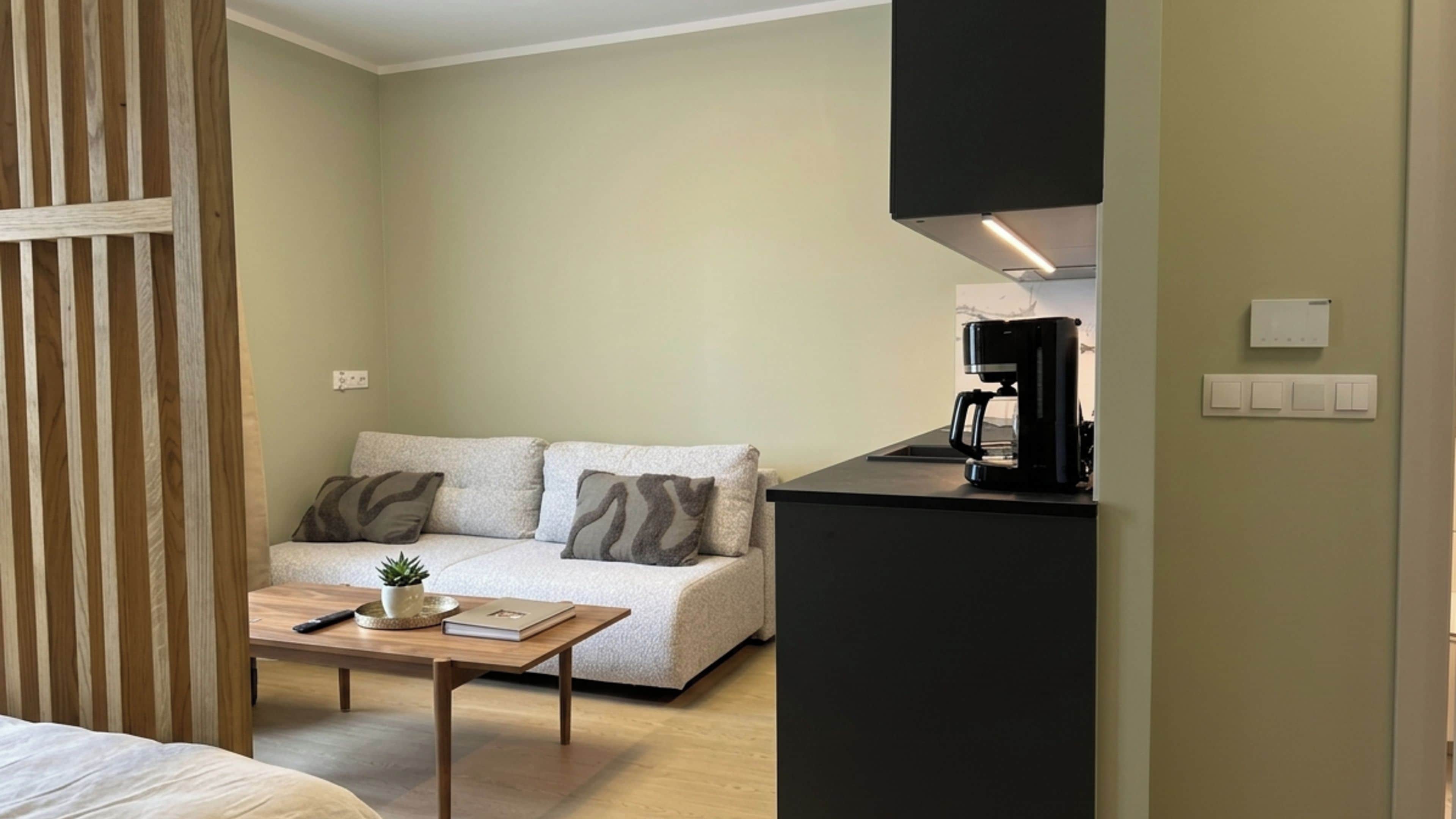 A small, modern room with a sofa, a coffee machine, and a table.