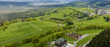 A rural landscape with a large green field, a building with a green roof, and a small parking area.