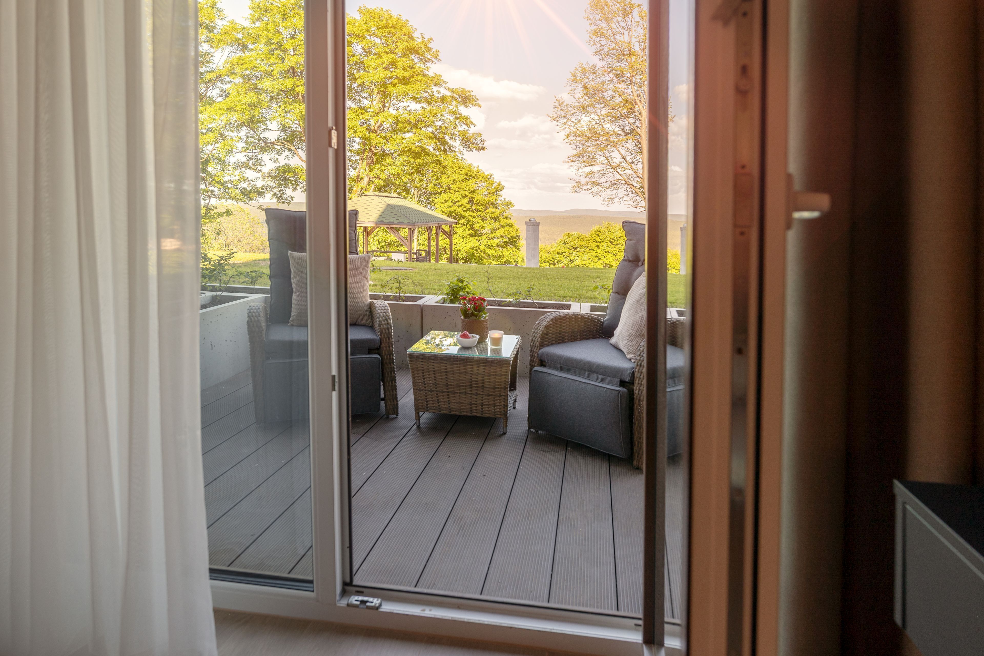 A deck with outdoor furniture, a covered seating area, and a view of a grassy landscape with trees.