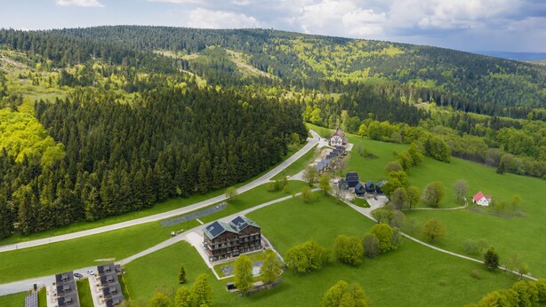 An aerial view of a rural area with a large building surrounded by green fields and dense forests. - Apartamenty Sun & Snow Willa Zieleniec (Duszniki Zdroj)
