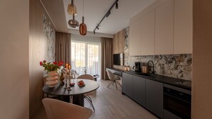 A modern kitchen with a built-in oven, a dining area with a round table and chairs, and a TV mounted above the counter. - Apartamenty Sun & Snow Willa Zieleniec (Duszniki Zdroj)