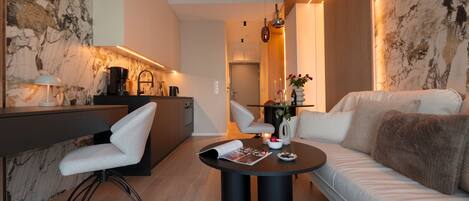 A modern living room with a sofa, a dining table, and a kitchen area.