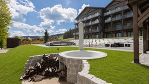 A modern building with a stone fireplace, a wooden deck, and a view of a mountain range. - Apartamenty Sun & Snow Willa Zieleniec (Duszniki Zdroj)