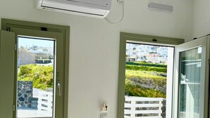 Una habitación con ventana, aire acondicionado, una puerta y vistas a una valla blanca y follaje exterior.