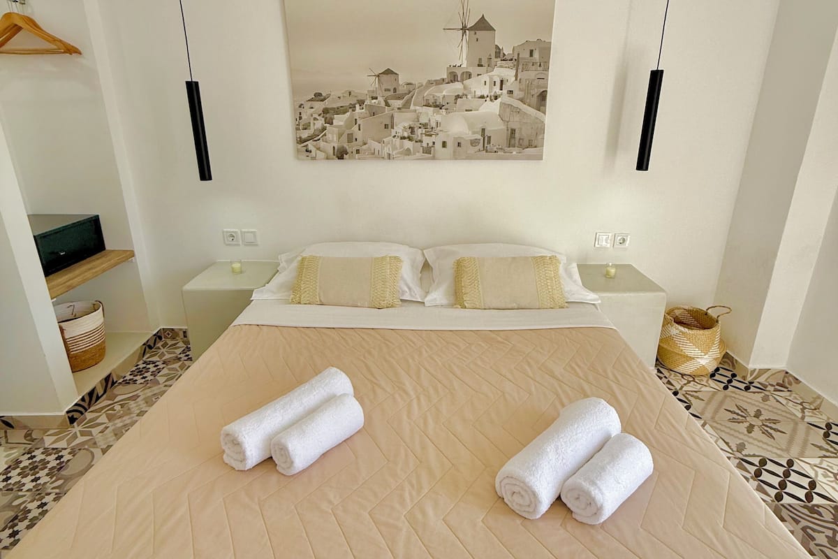 Une chambre d’hôtel avec un grand lit, deux tables de chevet, un tableau accroché au mur et un luminaire suspendu au plafond.