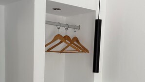 Una habitación con paredes blancas, un estante negro, perchas de madera y una lámpara colgante negra.
