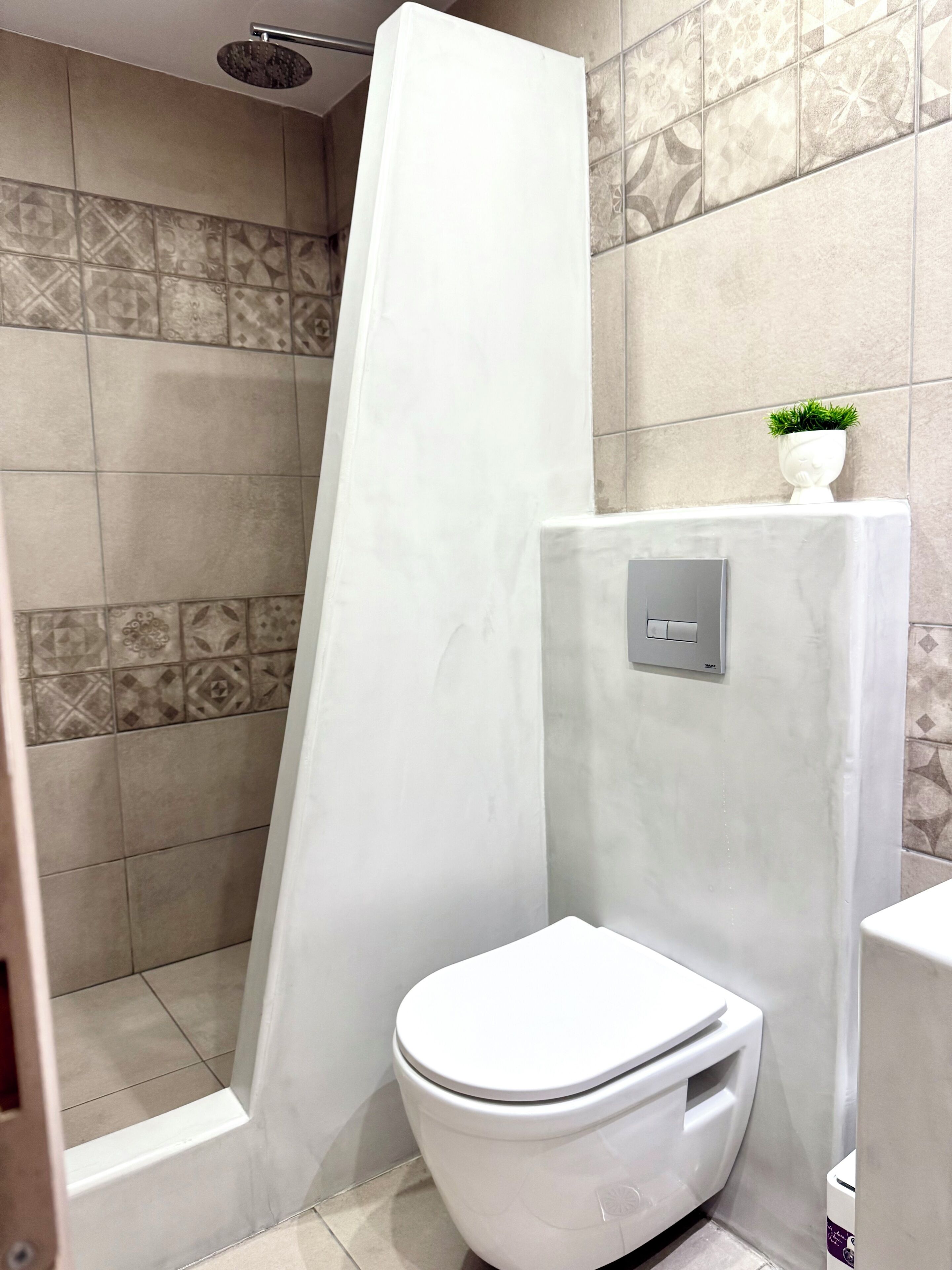 A bathroom with a shower enclosure, a toilet, and a wall-mounted control panel.