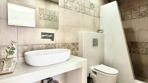 Un baño con un lavamanos blanco, un inodoro, una ducha y un espejo en la pared.