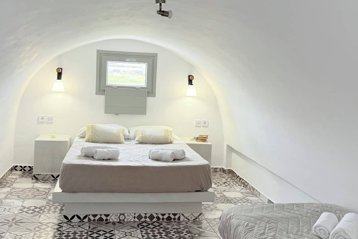 Une chambre à coucher accueillante et bien éclairée, avec un grand lit, un lit plus petit et un sol à motifs.