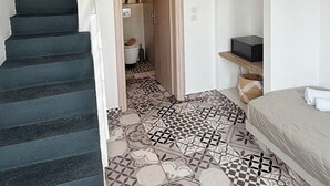 Una escalera conduce a un dormitorio en entrepiso con una cama, un perchero y un baño con inodoro y lavamanos.