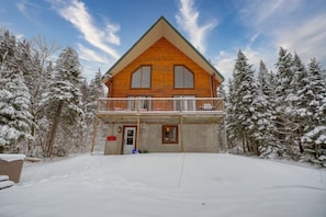Une cabane en bois à deux étages, dotée d’un balcon et entourée d’arbres couverts de neige.