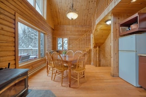 Ein Interieur einer Holzhütte mit Esstisch, Stühlen, einer Treppe und einem Kühlschrank.