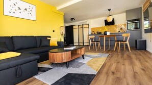 Ein modernes Wohnzimmer mit einem schwarzen Sofa, einem Holztisch und einer gelben Akzentwand.