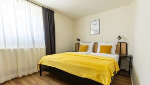 Ein Schlafzimmer mit einem Bett, einem Nachttisch, einer Lampe und einem Fenster mit Vorhängen.