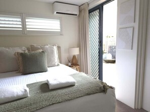A hotel room with a bed, a nightstand, a lamp, and a view of the outside. - Cerulean Beachfront - Unit 1 (Sunshine Coast)