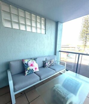 A balcony with a grey sofa, two pillows, and a glass table. - Cerulean Beachfront - Unit 1 (Sunshine Coast)