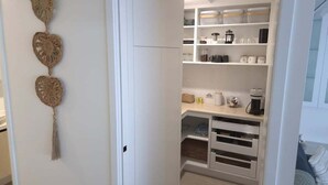 A white closet with shelves and drawers, a hanging decorative item, and a coffee maker. - Cerulean Beachfront - Unit 1 (Sunshine Coast)