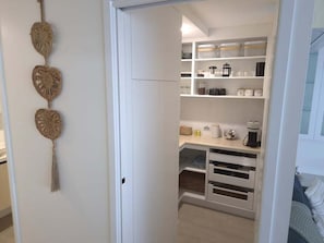 A white closet with shelves and drawers, a hanging decorative item, and a coffee maker. - Cerulean Beachfront - Unit 1 (Sunshine Coast)