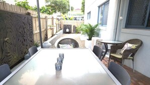 An outdoor patio with a glass-top table, chairs, and a small round table. - Cerulean Beachfront - Unit 1 (Sunshine Coast)