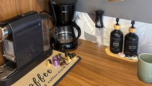 Een koffiehoek met een koffiezetapparaat, een molen en diverse koffiebekers en mokken.