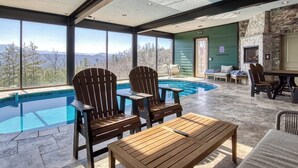 Uma área de piscina com cadeiras Adirondack, uma mesa de madeira e uma lareira de pedra.