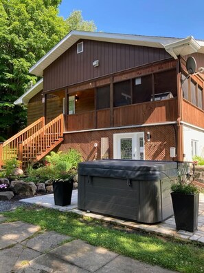 A two-story wooden house with a covered porch, a staircase, and a hot tub in the front yard. - Bécassines | Private Spa | Billiards | Waterfront (Nominingue)