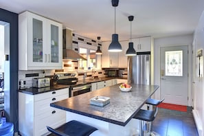 Una cocina moderna con armarios blancos, una isla central, electrodomésticos de acero inoxidable e iluminación colgante.